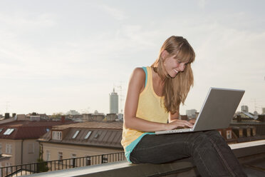 Germany, Bavaria, Munich, Young woman using laptop, smiling - SKF000398