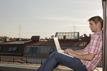 Germany, Bavaria, Munich, Young man with laptop on rooftop - SKF000401