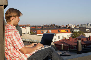 Deutschland, Bayern, München, Junger Mann mit Laptop auf Dachterrasse - SKF000402