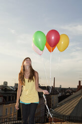Deutschland, Bayern, München, Junge Frau mit Luftballons auf einem Dach, lächelnd - SKF000374
