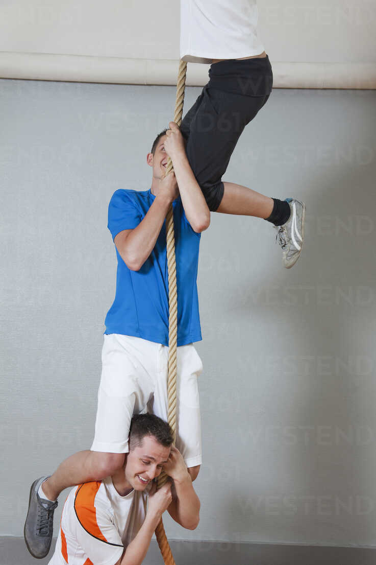 Germany, Berlin, Young men and woman climbing rope in school gym