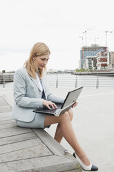 Germany, Hamburg, Businesswoman smiling at harbour using laptop - WESTF015432