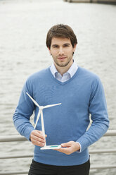 Germany, Hamburg, Businessman holding wind turbine, portrait - WESTF015448