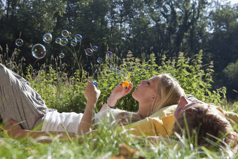 Germany, Dortmund, Young woman blowing bubble with lying on man - SKF000272