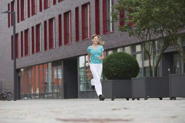 Deutschland, Köln, Junge Frau joggt, lächelnd - SKF000298