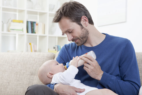 Deutschland, Bayern, München, Vater füttert kleinen Jungen (6-11 Monate) im Wohnzimmer mit Milch - RBF000411