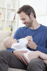 Germany, Bavaria, Munich, Father feeding milk to baby boy (6-11 Months) in living room - RBF000327