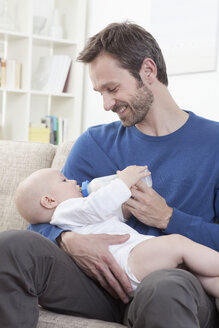 Deutschland, Bayern, München, Vater füttert kleinen Jungen (6-11 Monate) im Wohnzimmer mit Milch - RBF000327