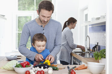 Germany, Bavaria, Munich, Father and son (2-3 Years) chopping pepper and mother in background - RBF000362