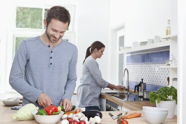 Germany, Bavaria, Munich, Man chopping courgette in kitchen, woman in background - RBF000364