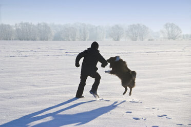 Germany, Vechelde, Boy playing with australian shepherd in snow - HKF000357