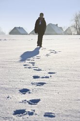 Deutschland, Vechelde, Junge geht im Schnee mit Fußspuren im Vordergrund - HKF000358