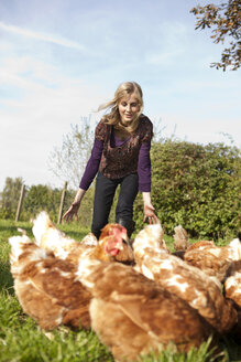 Deutschland, Sachsen, Junge Frau fängt Hühner auf dem Bauernhof - MBF001036