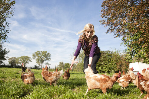 Deutschland, Sachsen, Junge Frau fängt Hühner auf dem Bauernhof - MBF001037