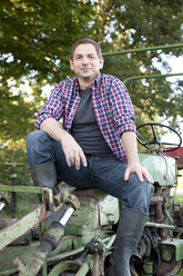 Germany, Saxony, Mature man sitting on tractor, smiling, portrait - MBF001068