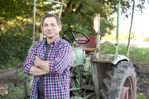 Germany, Saxony, Mature man standing by tractor, smiling - MBF001069