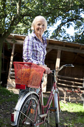 Deutschland, Sachsen, Seniorin mit Fahrrad auf dem Bauernhof - MBF001096