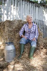 Deutschland, Sachsen, Ältere Frau im Gras sitzend mit Milchkanne - MBF001100