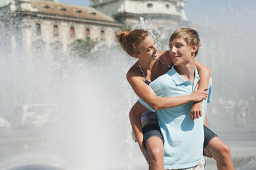 Germany, Munich, Karlsplatz, Young man carrying woman on piggy back - RNF000413