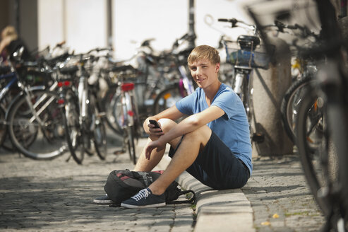 Germany, Munich, Karlsplatz, Young man with mobile, portrait, smiling - RNF000399