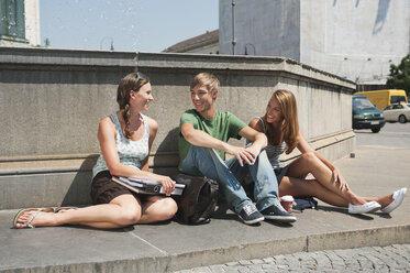 Germany, Munich, Young man and young women sitting at fountain in university - RNF000385