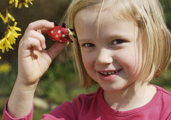 Deutschland, Bayern, Mädchen (6-7 Jahre) hält Osterschokoladenkäfer, Porträt, lächelnd - WBF000070