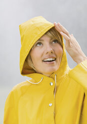 Frau in gelbem Regenmantel schaut auf und lächelt - WBF000781