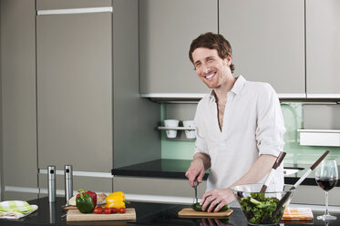 Germany, Hamburg, Man in kitchen cutting cucumber - WESTF015554