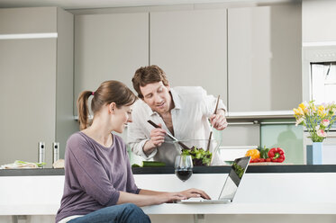 Deutschland, Hamburg, Mann bereitet Salat vor, Frau benutzt Laptop in der Küche - WESTF015572