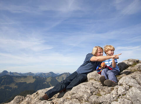 Deutschland, Bayern, Vater und Sohn (4-5 Jahre) sitzen auf einem Berggipfel, lizenzfreies Stockfoto
