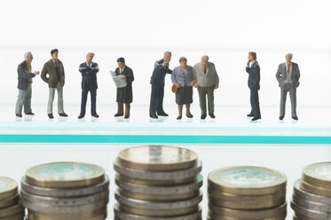 Businesspeople figurines standing with euro coins in foreground - ASF004181