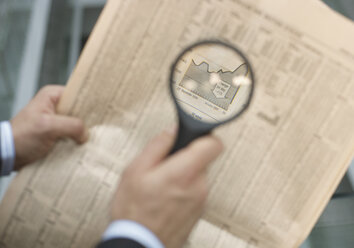 Man holding a magnifying glass over a newspaper - WBF000819