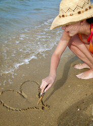Croatia, Zadar, Young woman drawing heart-shaped on sand at beach - HSIF000043