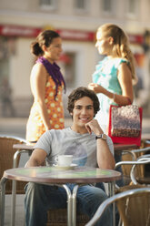Deutschland, München, Junger Mann im Cafe lächelnd mit Freunden im Hintergrund - RNF000478