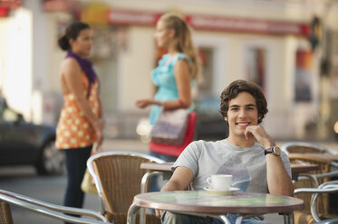 Deutschland, München, Junger Mann im Cafe lächelnd mit Freunden im Hintergrund - RNF000477
