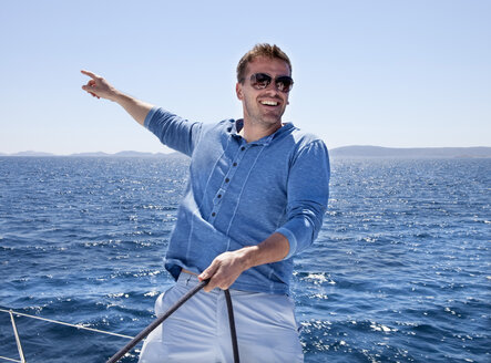 Kroatien, Zadar, Junger Mann zeigt von Segelboot, lächelnd - HSIF000079