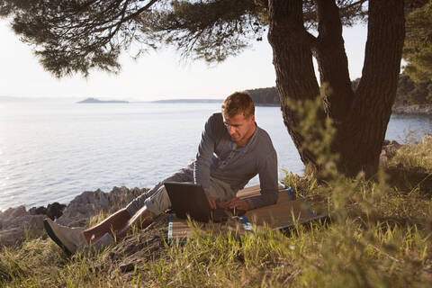 Kroatien, Zadar, Junger Mann mit Laptop am Strand, lizenzfreies Stockfoto