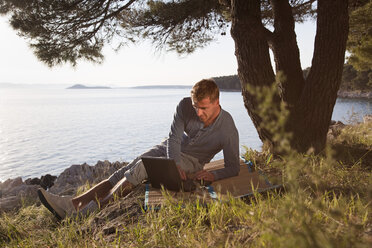 Croatia, Zadar, Young man using laptop at the beach - HSIF000098