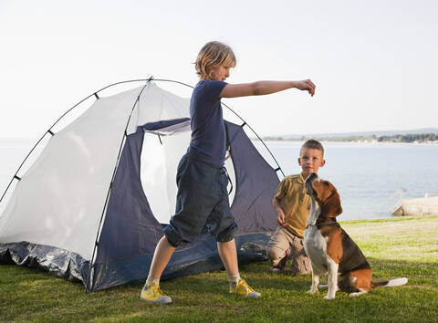 Kroatien, Zadar, Mädchen und Junge spielen mit Hund vor einem Zelt am Strand, lizenzfreies Stockfoto