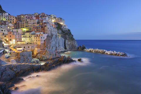 Italien, Cinque Terre, Provinz La Spezia, Manarola, Ligurien, Blick auf ein traditionelles Fischerdorf in der Abenddämmerung, lizenzfreies Stockfoto