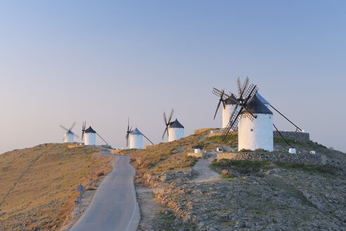 Spanien, Provinz Toledo, Kastilien-La Mancha, Reihe von Windmühlen mit Landstraße bei Sonnenaufgang - RUEF000611