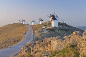 Spain, Toledo Province, Castile-La Mancha, Row of windmills with rural road at sunrise - RUEF000612