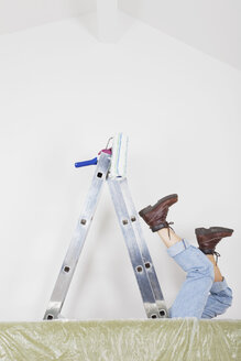 Germany, Cologne, Mature woman fallen down from step ladder during painting living room - GWF001355