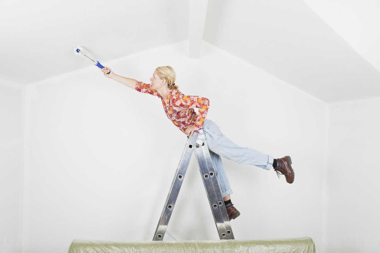 Germany, Cologne, Mature woman balancing on ladder during painting