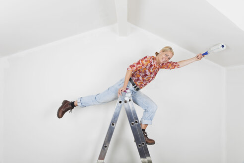 Deutschland, Köln, Ältere Frau balanciert auf Leiter beim Streichen des Giebeldachs - GWF001363