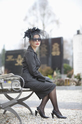 Deutschland, Bayern, Junge Frau sitzt auf Bank auf Friedhof - MAEF002734