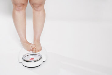 Young woman standing on bathroom scales - PDF000141