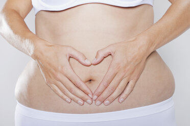 Germany, Cologne, Young woman making heart shape with hands on stomach - PDF000059