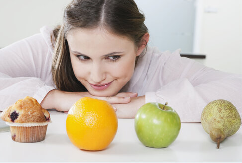 Deutschland, Köln, Junge Frau verwirrt zwischen Obst und Süßigkeiten - PDF000144