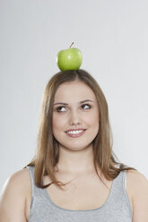 Junge Frau mit grünem Apfel auf dem Kopf, lächelnd - PDF000090